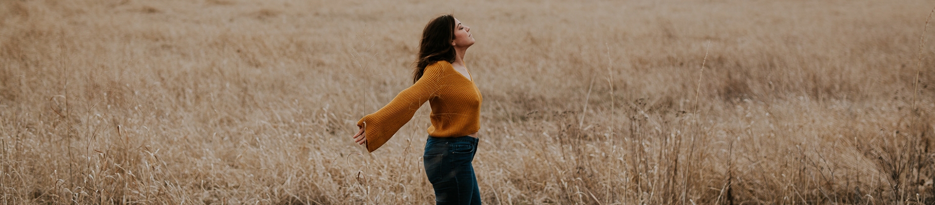 A women in a orange jumper stood in a field with her arms out wide A women in a orange jumper stood in a field with her arms out wide