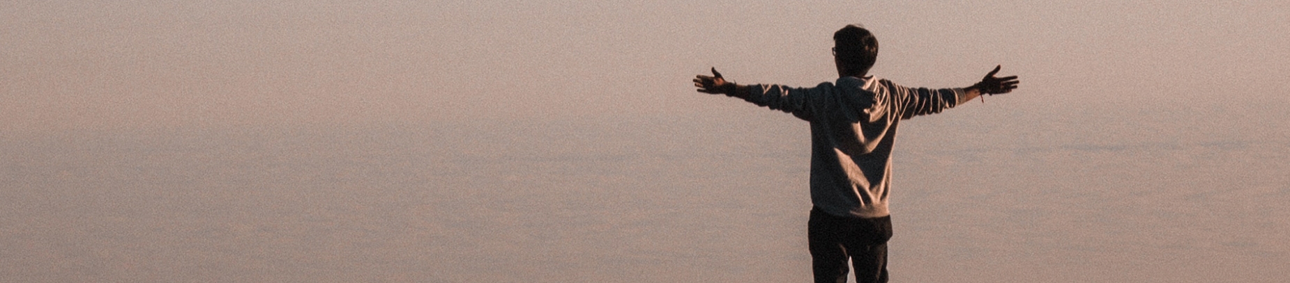 A man stood looking over a cliff with his arms open wide A man stood looking over a cliff with his arms open wide
