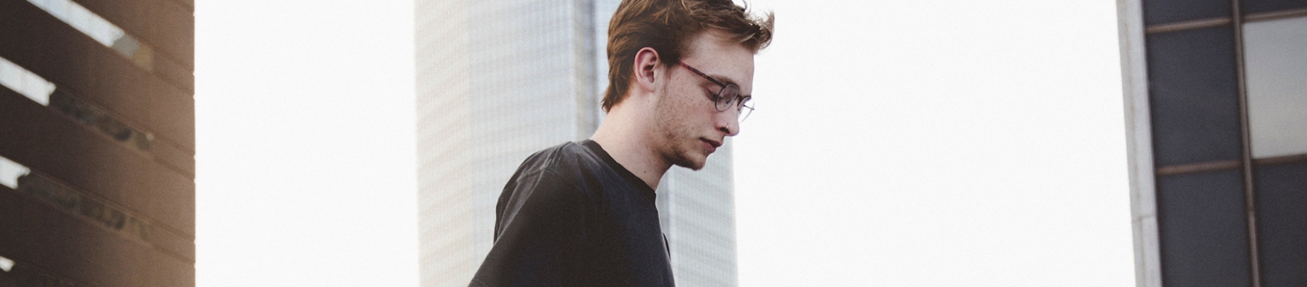 A young guy looking down at the ground with a skyline of buildings behind him A young guy looking down at the ground with a skyline of buildings behind him