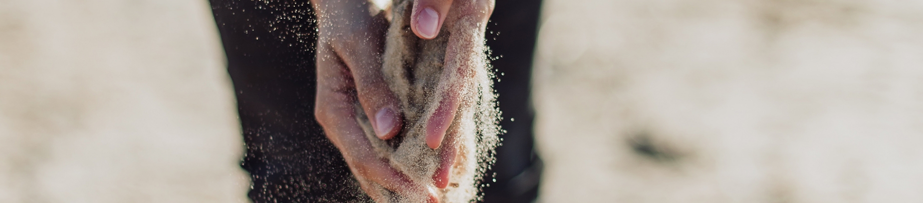 A person tipping sand through their hands on a beach