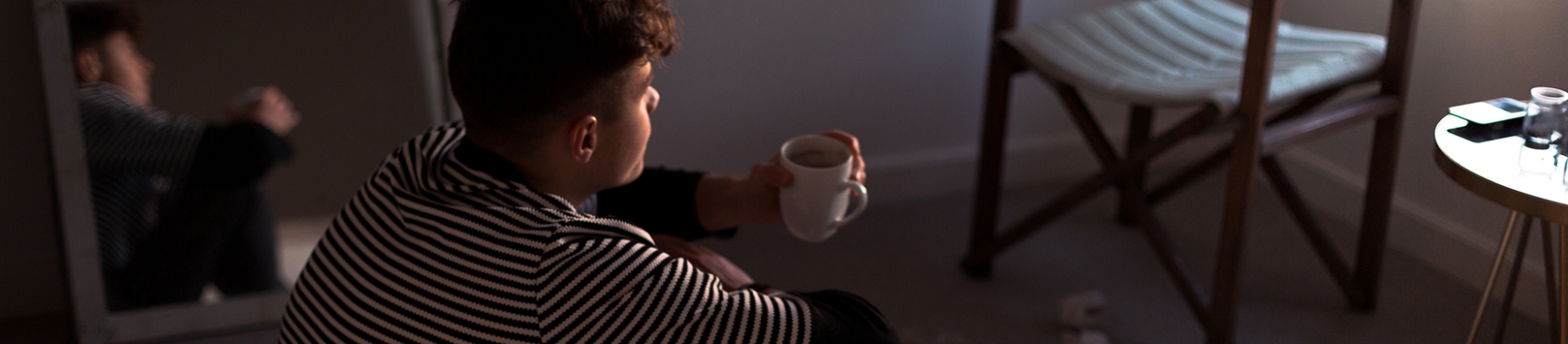 A guy sat on the floor of his room holding a mug of tea A guy sat on the floor of his room holding a mug of tea