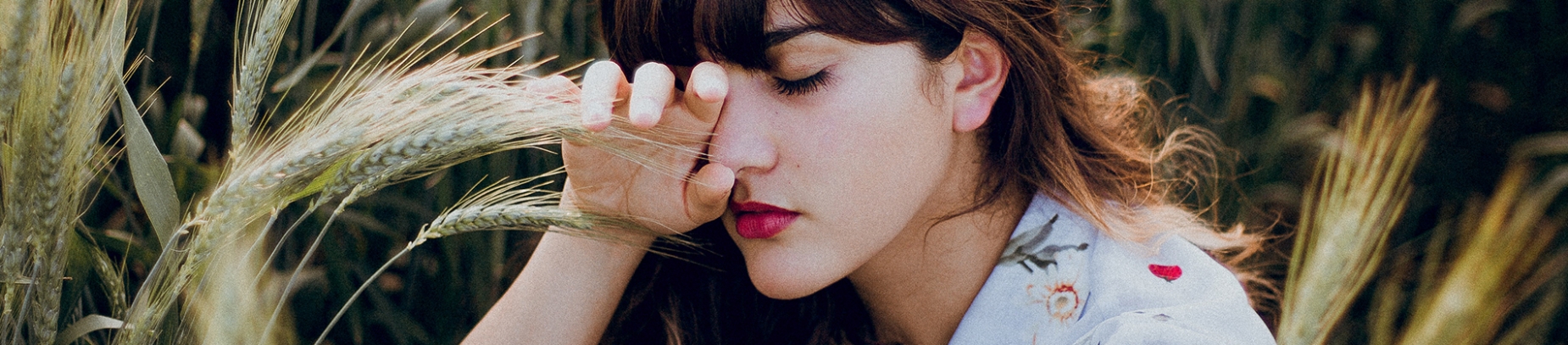 A women sat in a corn field with her eyes closed and her hand over one eye A women sat in a corn field with her eyes closed and her hand over one eye