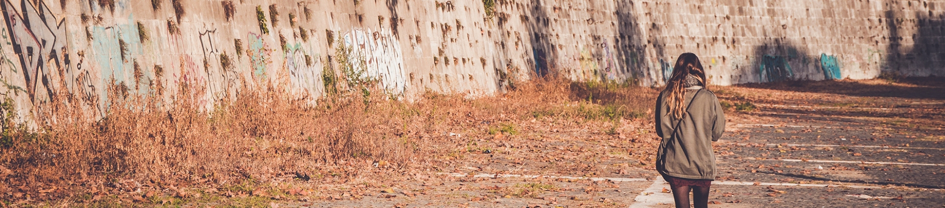 A women walking down a large path with a wall and shrubs down one side A women walking down a large path with a wall and shrubs down one side