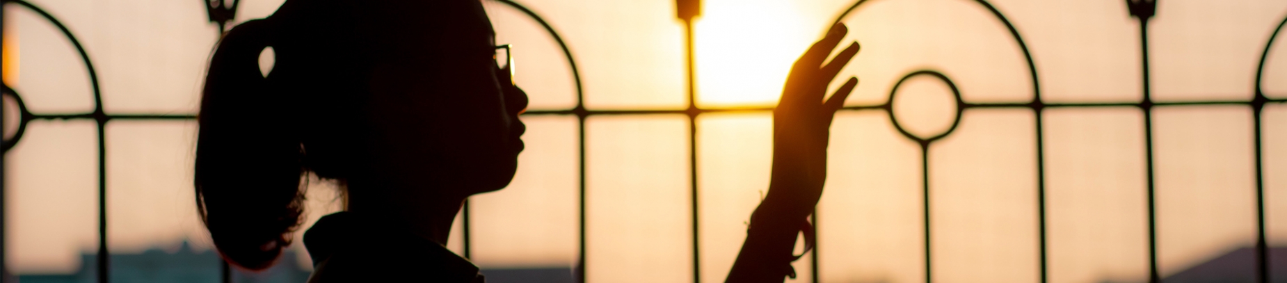 A woman with her hand in the air in front of a gate and the sunset A woman with her hand in the air in front of a gate and the sunset