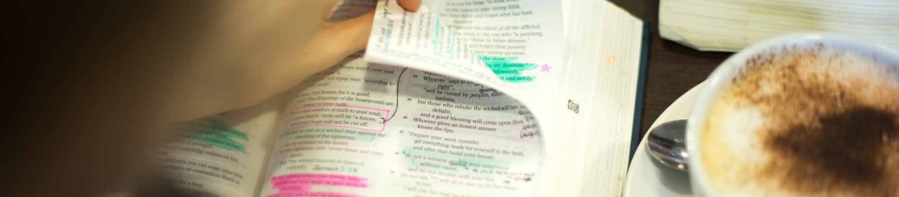 A girl reading Bible full of notes and highlights next to a cup of coffee