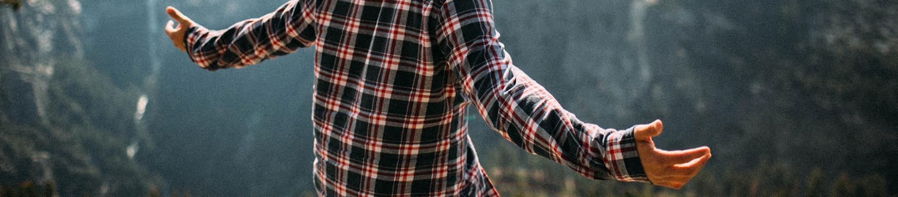 A man in a checked shirt with his arms open looking out over a mountain range A man in a checked shirt with his arms open looking out over a mountain range