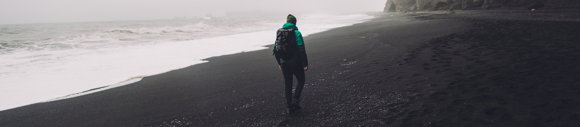A man walking down a grey looking beach A man walking down a grey looking beach