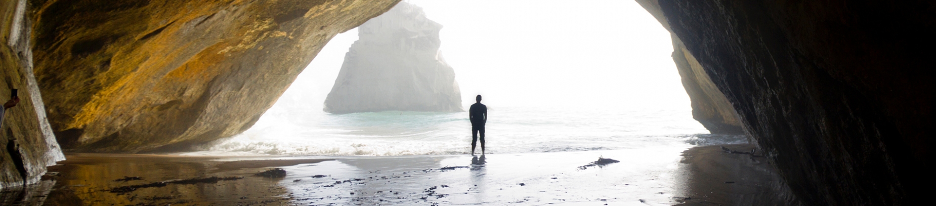 A mean walking out of a large cave into the sea