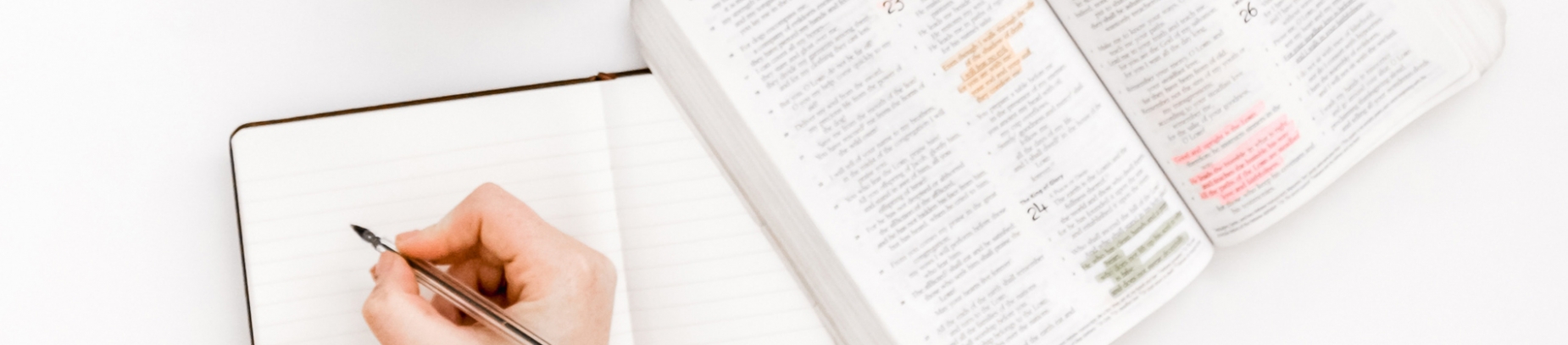 Someone writing in a notebook next to a open bible with highlighted verse Someone writing in a notebook next to a open bible with highlighted verse