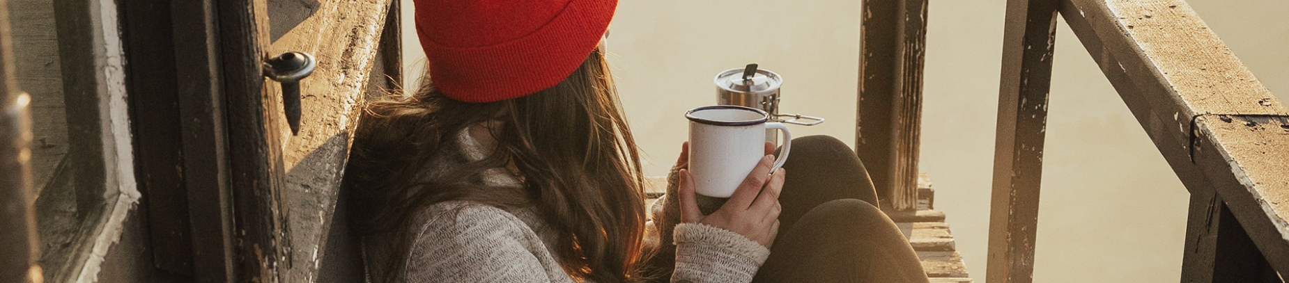 A women sat looking out on a wooden balcony holding a mug A women sat looking out on a wooden balcony holding a mug