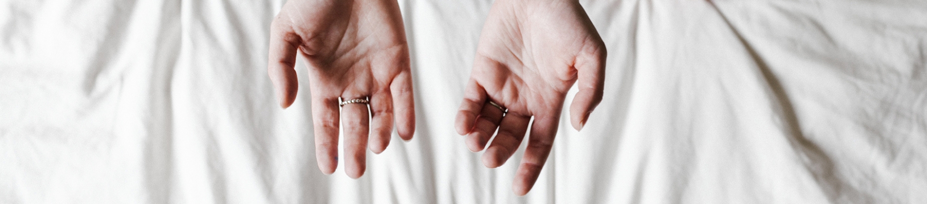 Hands open in prayer over a white bed sheet