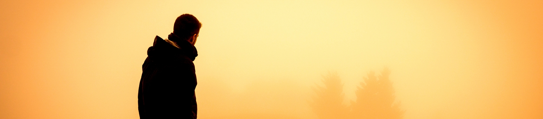 A man wearing a dark coat looking over a sunrise A man wearing a dark coat looking over a sunrise