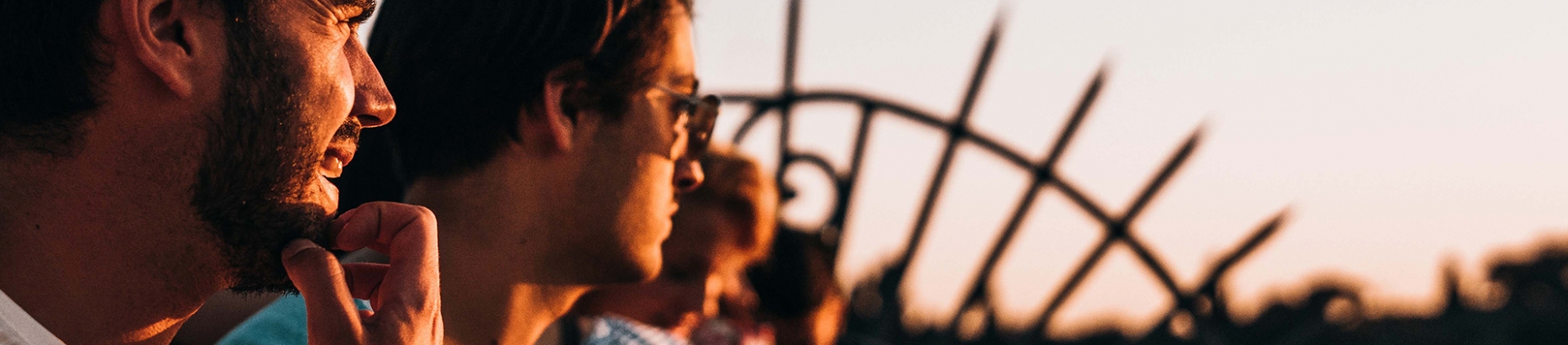 A group of guys sat looking towards a sunset
