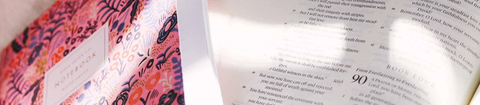 Open bible with a pink notebook ontop