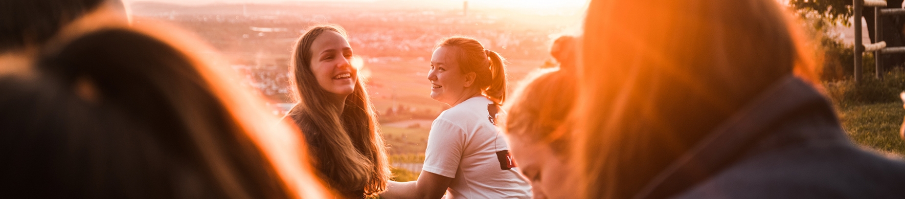 Friends sat together, talking and laughing, in a park at sunset Friends sat together, talking and laughing, in a park at sunset