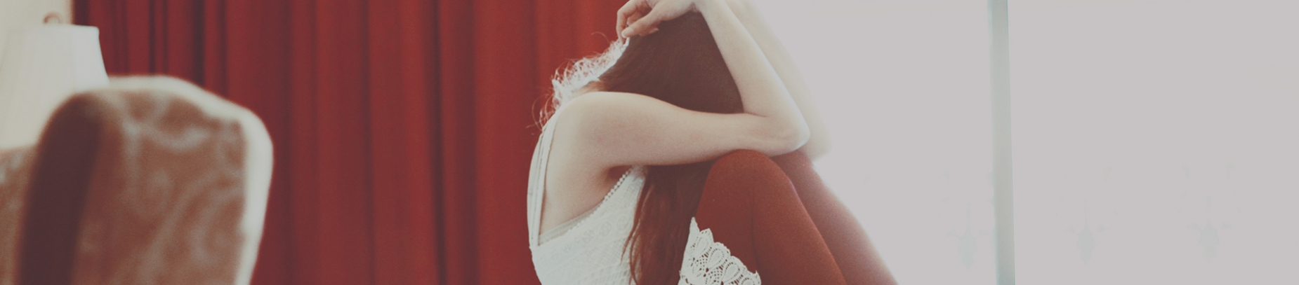 A women sat curled up on her bed A women sat curled up on her bed