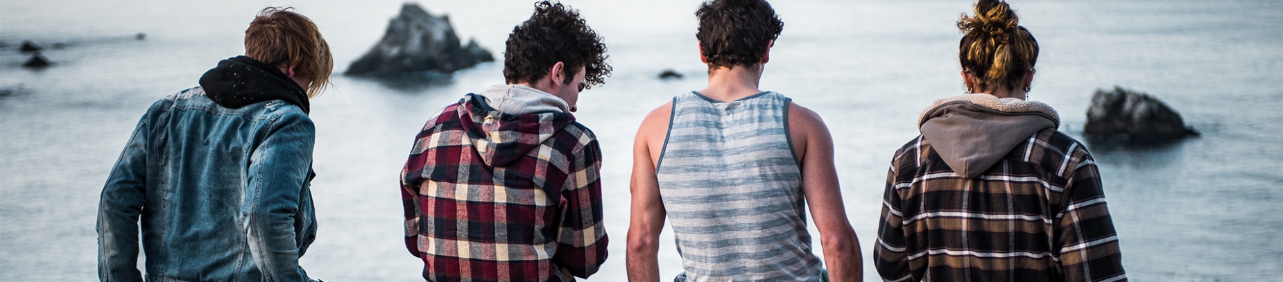 A group of friends sat on a wall looking out over to sea A group of friends sat on a wall looking out over to sea