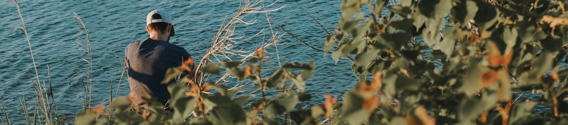A guy sat down by a river with bushes behind him A guy sat down by a river with bushes behind him