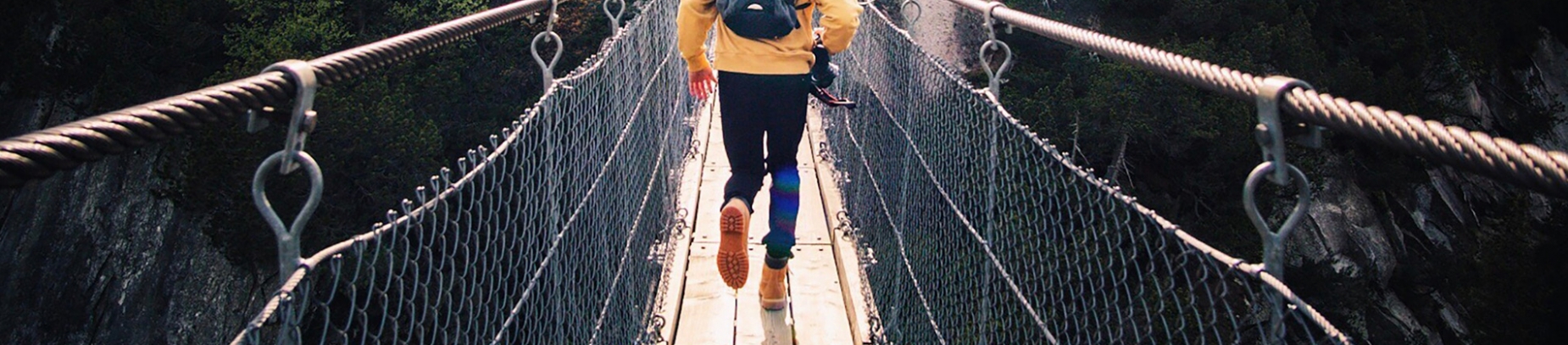 A man in a yellow hoodie running across a rope bridge A man in a yellow hoodie running across a rope bridge
