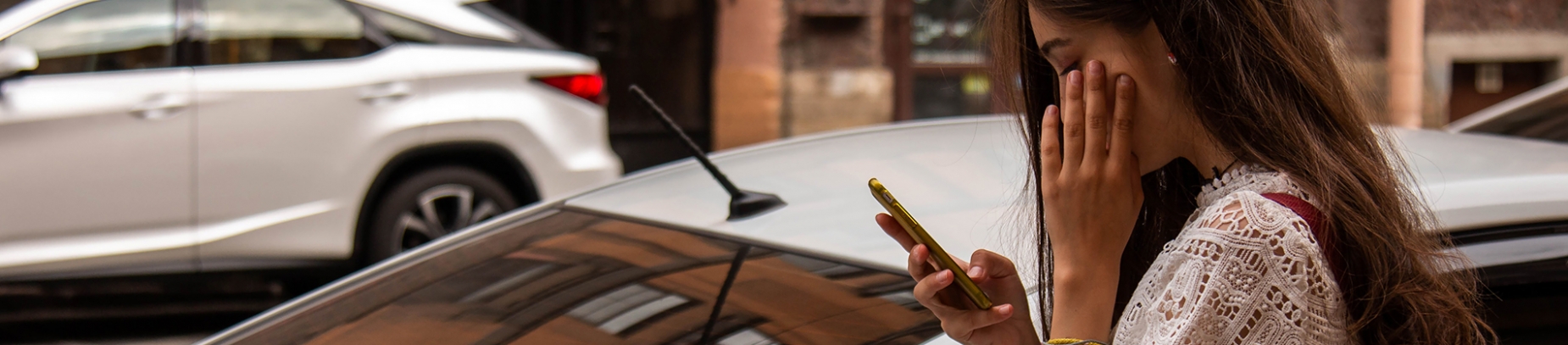 A girl stood on the side of the road in front of a car, on her phone A girl stood on the side of the road in front of a car, on her phone