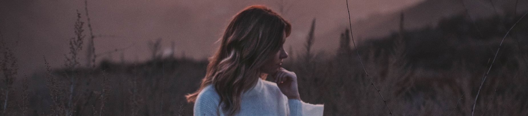 A girl stood in a field at dusk, looking down to the ground