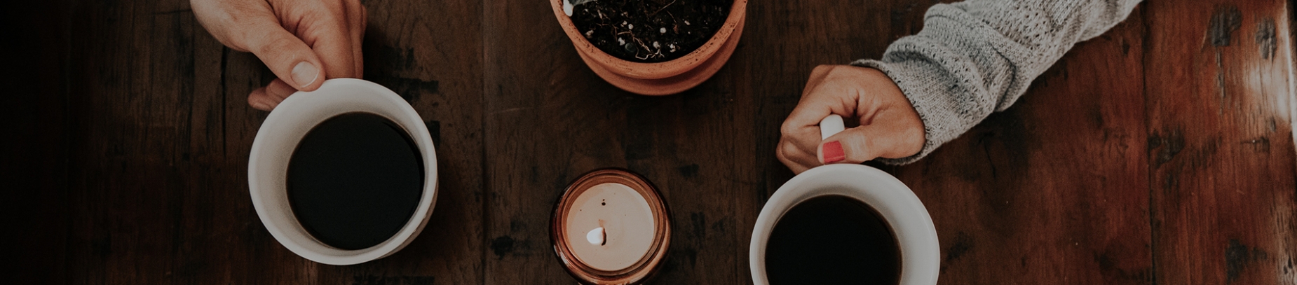 Two people sat with cups of coffee on a wooden table