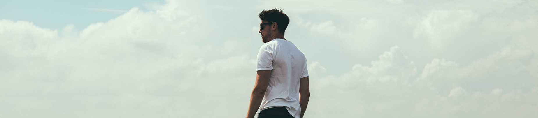 A man stood looking sidewards with the clouds and sky behind him A man stood looking sidewards with the clouds and sky behind him
