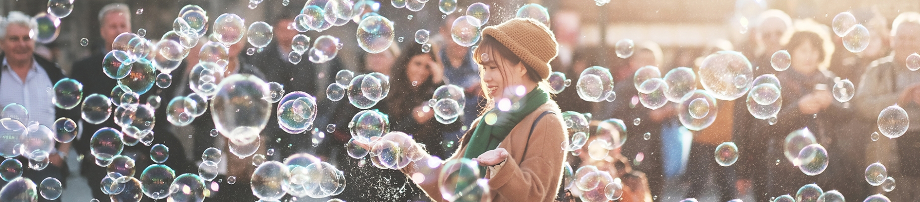 A girl stood in a crowd of people surrounded by bubbles