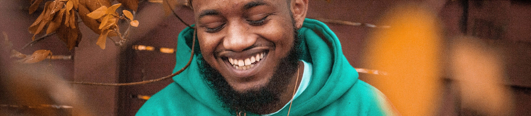 A man surrounded by autumn leaves in a green hoodie smiling A man surrounded by autumn leaves in a green hoodie smiling