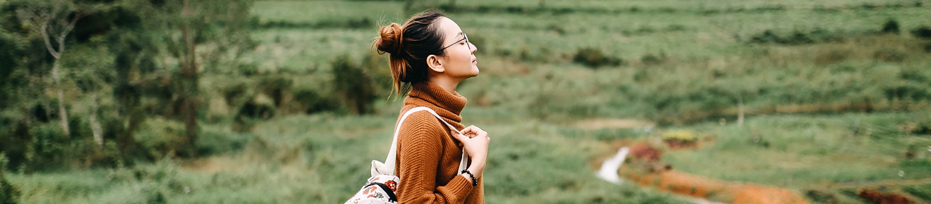 A women with a backpack stood in a field with her eyes closed A women with a backpack stood in a field with her eyes closed
