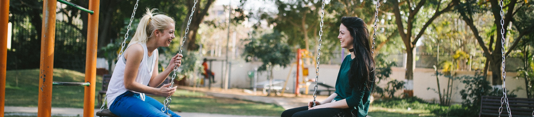 Two girls talking and laughing on park swings