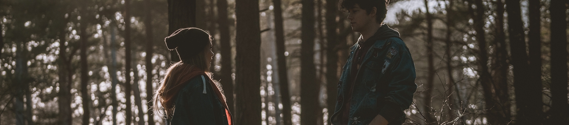 A girl and guy facing each other with a forest behind them A girl and guy facing each other with a forest behind them
